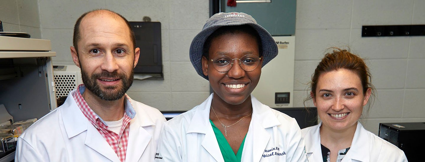 two students and a laboratory technician wearing lab coats in a laboratory