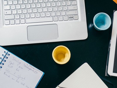 top view of office desk table with organizer notebook tablet pencil and cups of coffee