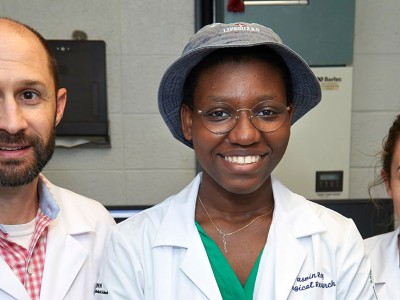 Two students and a laboratory technician wearing lab coats in a laboratory